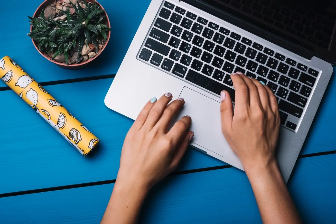 Руки используют ноутбук на синем столе.